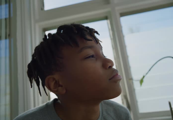 Boy with gray shirt and dreadlocks closes his eyes and opens his eyes in room
