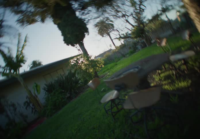 A backyard with green grass a table and chair set behind the house as the camera tips over