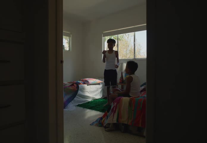 Two boys in their bedroom one sitting on a bed and the other lighting a match standing in the room