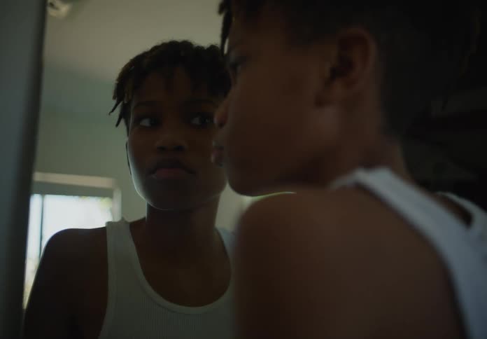 Boy with dreadlocks and white undershirt looks in a mirror in room