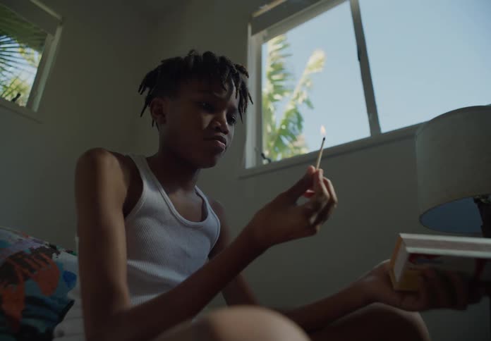 A boy sitting opening a match box and striking a flame