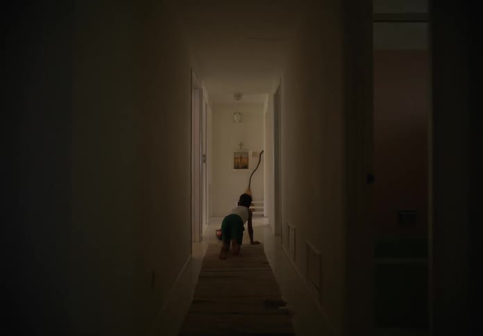 A young boy on his knees crawling down a hallway with a toy