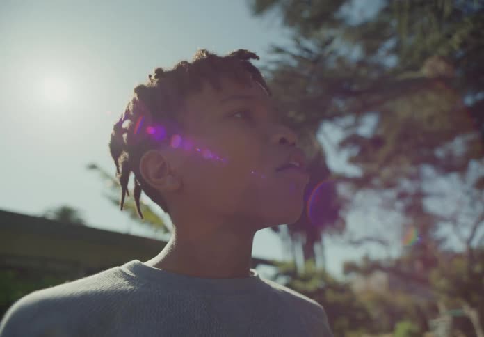 Boy with dreadlocks and blue shirt looks around and laugh in the yard