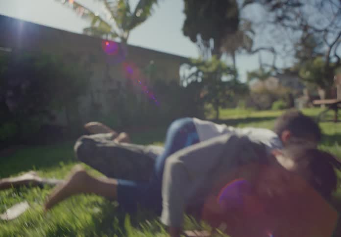 Younger brother tackles his older sibling as they play in yard on sunny day