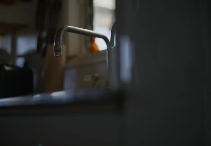 Water drips from the kitchen faucet as light shines in fron the window