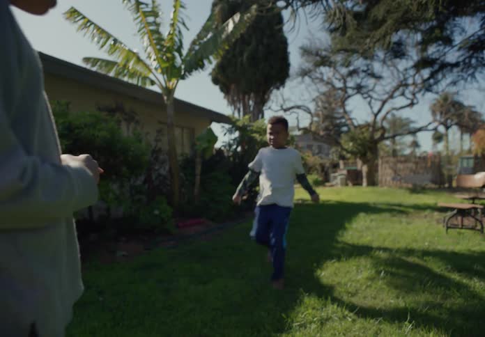 Older sibling claps as younger brother runs across yard to him and they fist bump
