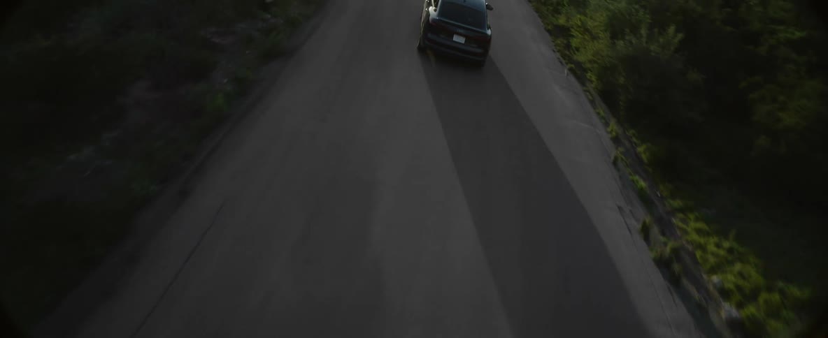 A car travels along a winding road through dense vegetation in the countryside during the day