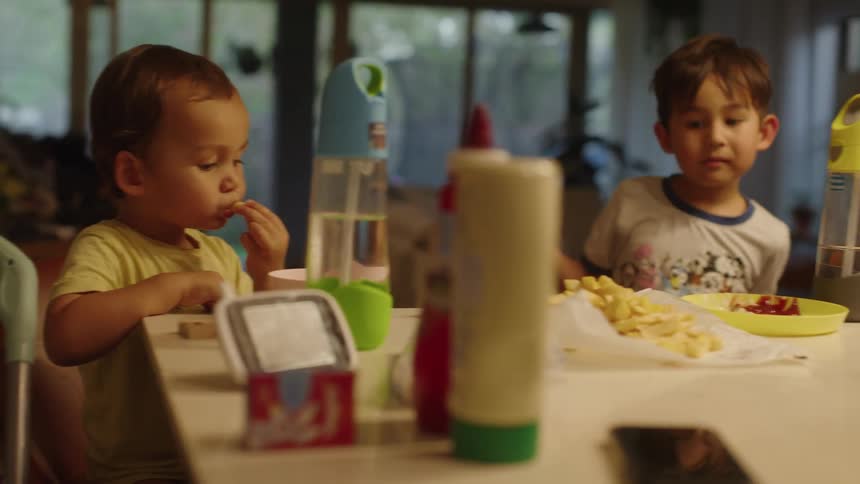 Two young boys sitting at a table eating next to each other