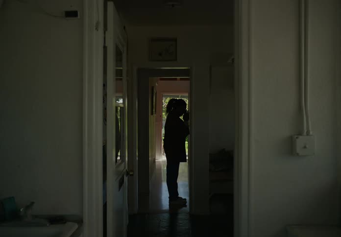 A woman standing in a hallway then walking away being follow by her sons