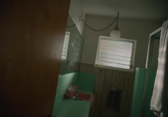 A teal tiled bathroom with a pink sink and a round light fixture hanging from the ceiling