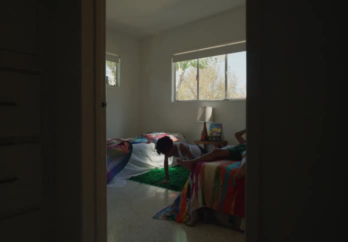 A young boy sitting on a bed moves to the floor and starts doing pushups