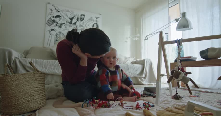 A mother playing with her baby daughter on the floor on a baby blanket