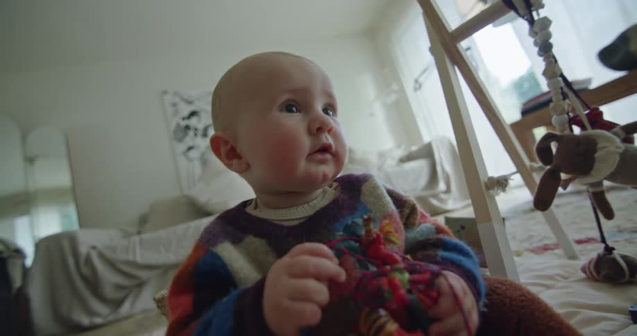 A close up of a babys face as she sits on the floor playing with a toy