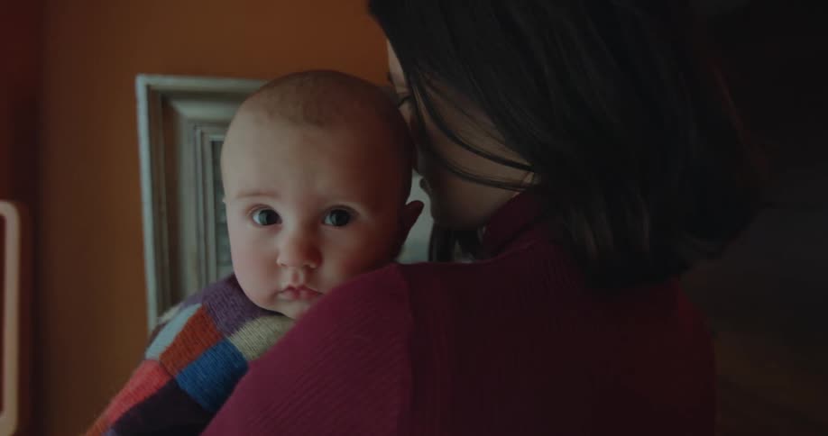 A mother holding her baby girl while she sways back and forth and the baby looks around