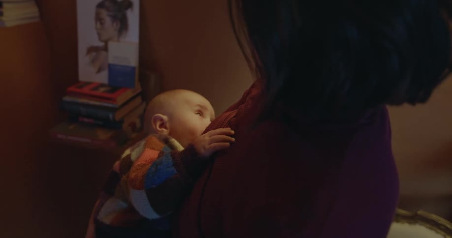 Mother stands on the living room breastfeeding her newborn son at home