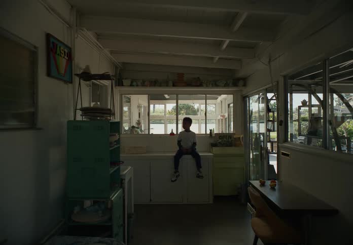 A boy sits on a counter indoors and looks to the side