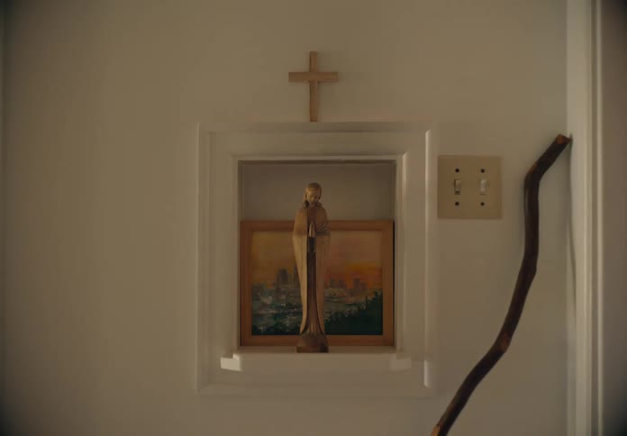 A framed picture with a statue and cross on a wall as a child walks by brushing his teeth