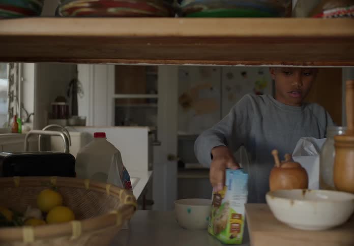 A boy is grabbing a bowl and taking groceries out of a bag including milk cereal donuts and granola bars