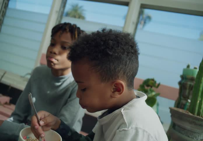 Two brothers sitting in the sun room one eating a bowl of breakfast cereal probably watching tv