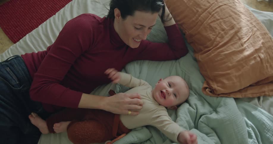 Mother rubs the belly of his happy newborn son in the bed at home