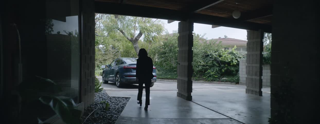 Following a welldressed person walking out of their large modern home toward an audi etron