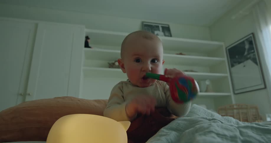 Infant baby sitting up on couch playing with toys and putting them in mouth