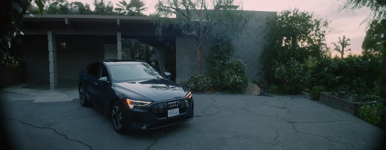 A young woman walks out into her driveway and gets into an expensive black sedan