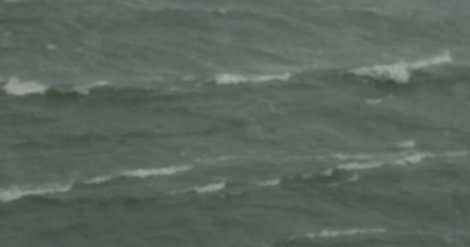A water spotted window and waves rolling in gray water
