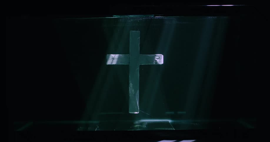 A wooden cross rests on the front of a black box while spotlights swirl around it