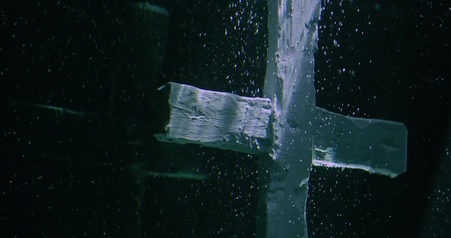 Light shines on a white wooden cross underwater as air bubbles float upward