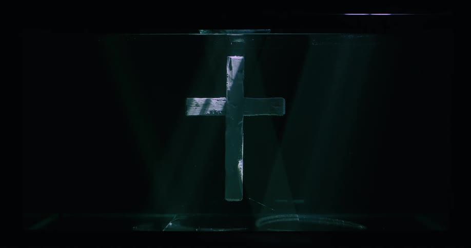 A black covered in black velvet and a white cross in shadow with streams of light coming in on it