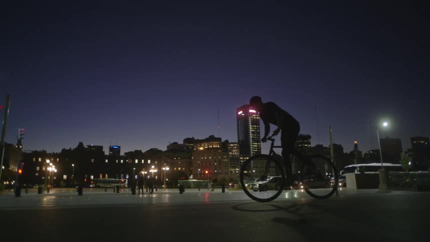 A man rides his bicycle down a trail past the city skyline
