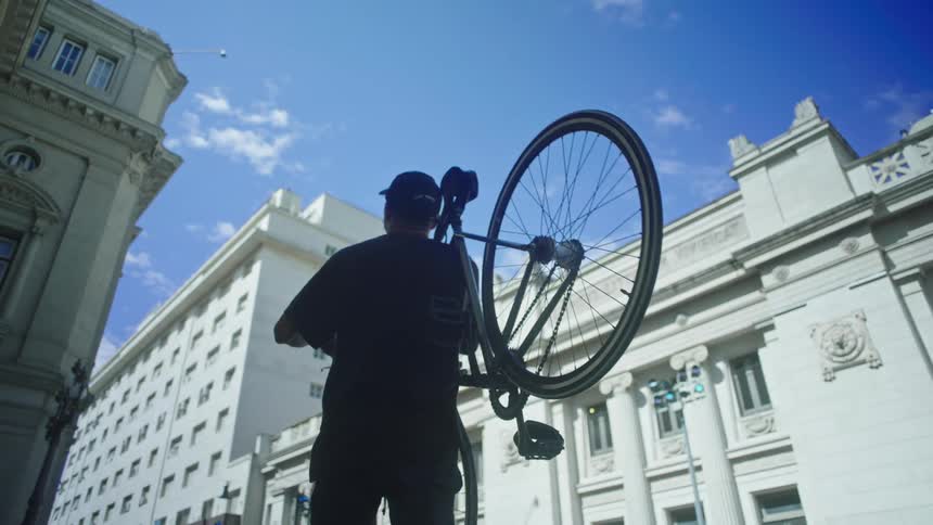 A man is standing in town holding a bicycle as he turns to look up at a building