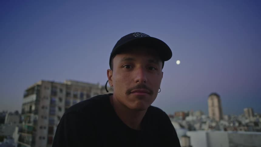 A man smiles wide while sitting on the rooftop of a downtown building