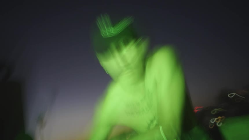 Shirtless man sitting on roof with city and sunset in background long exposure low frame rate streaking
