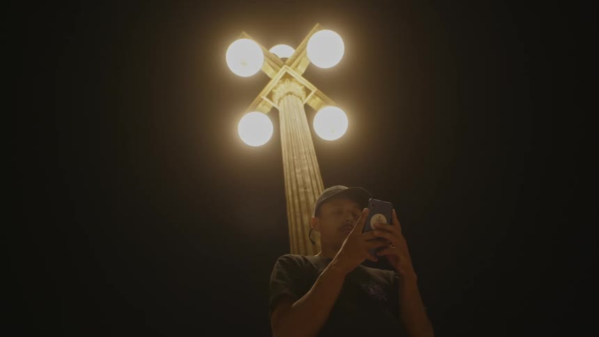 A man is using his cell phone under the lamp post