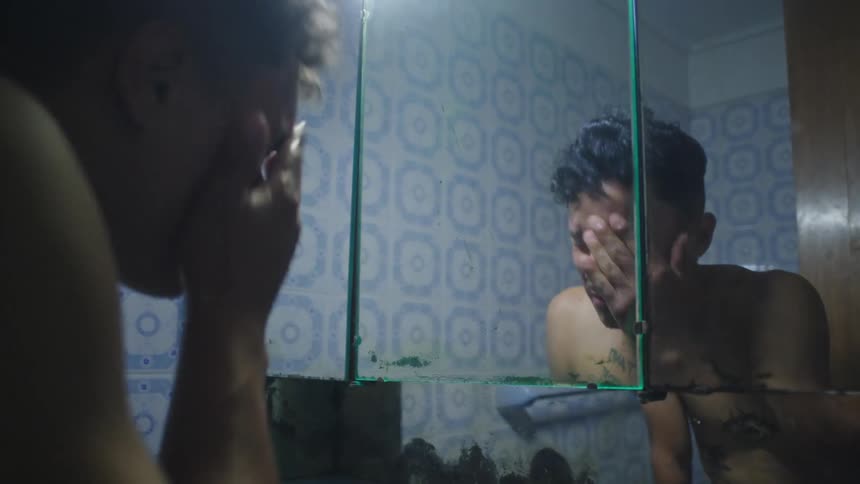 A man is washing his face in the bathroom sink and he looks in the mirror