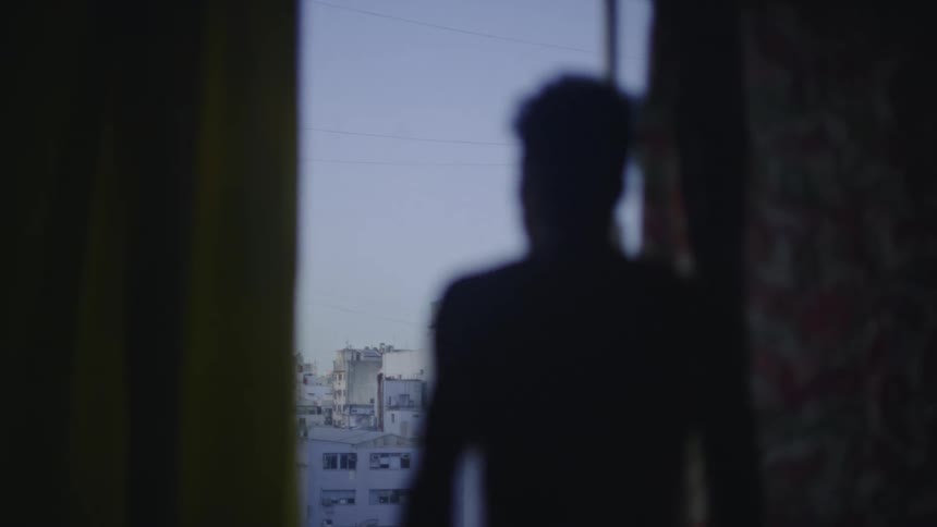 A man stands at his window and looks at the buildings below