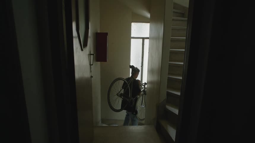 A man carrying a bicycle over his shoulder walking down stairs