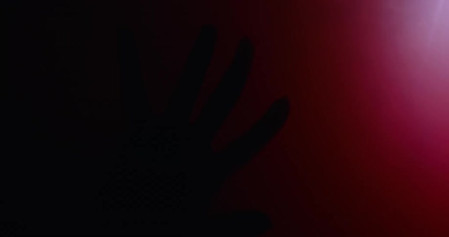 A silhouette of a persons hand wide open against a surface with red lights in the back