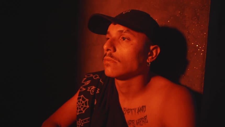 A man is sitting by a wall and wearing a hat in the red light