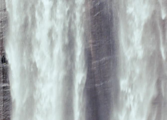 Water foams white as the waterfall flows down textured cliff