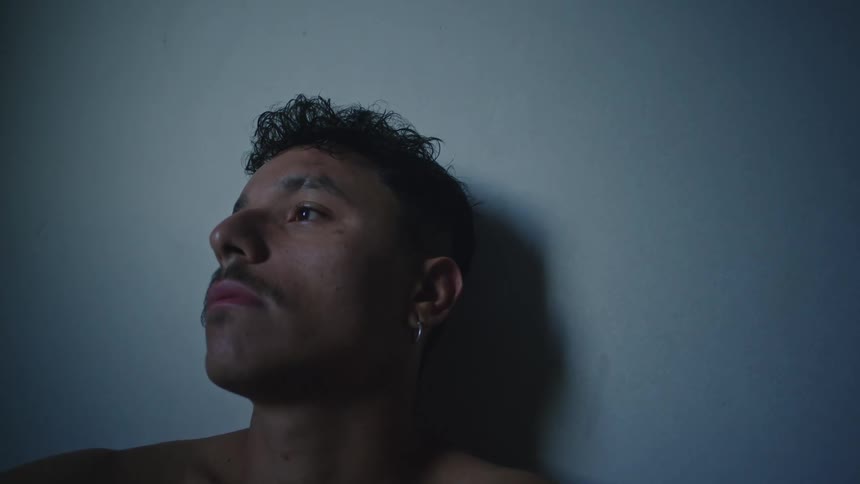 A close up of a mans face sitting against a wall and looking sad