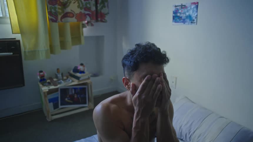 Man sitting up in bed just woke up yawning rubbing face stretching neck