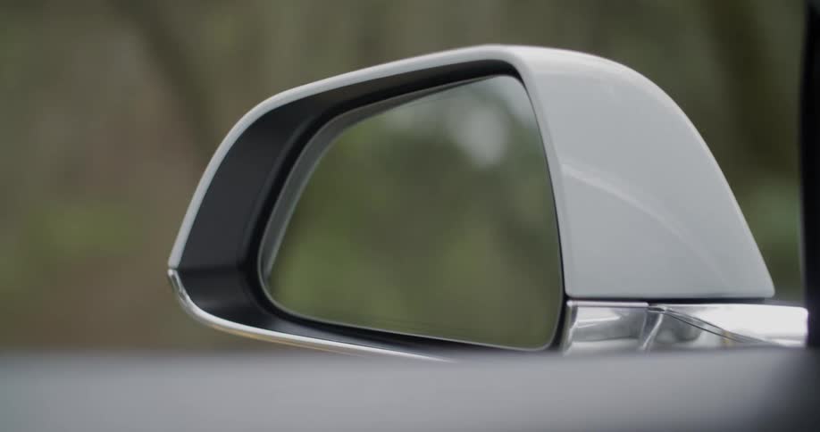 Passing trees are seen in the side view mirror of an automobile as it travels on a street through the woods