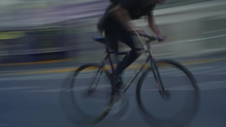 A man rides his bicycle on a city street behind a car as a pedestrian crosses the street