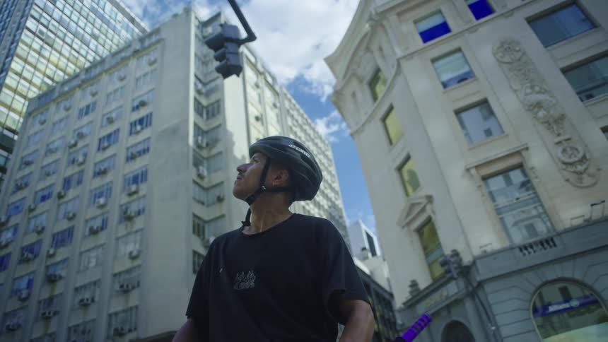 A man stands in front of apartment buildings with his bike and looks around at the buildings