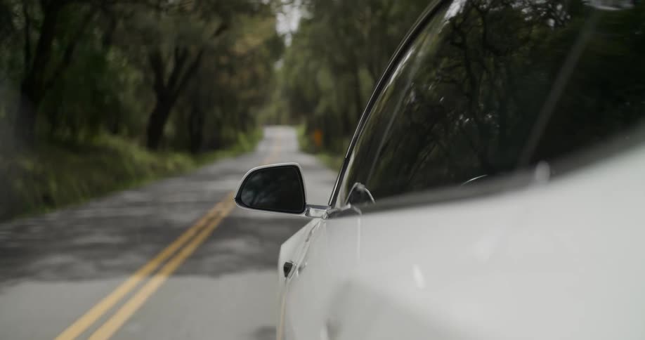 An electric car is driving on a road in a wooded area