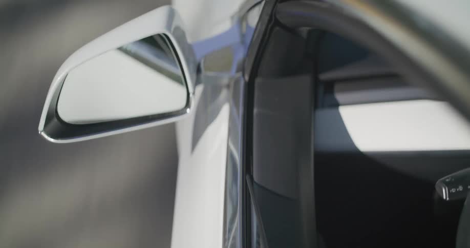 A car window and side mirror as a person rolls down the window and sticks their hand out
