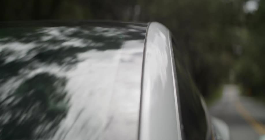 Exterior of car upper right corner of driver side driving down rural road surrounded by trees